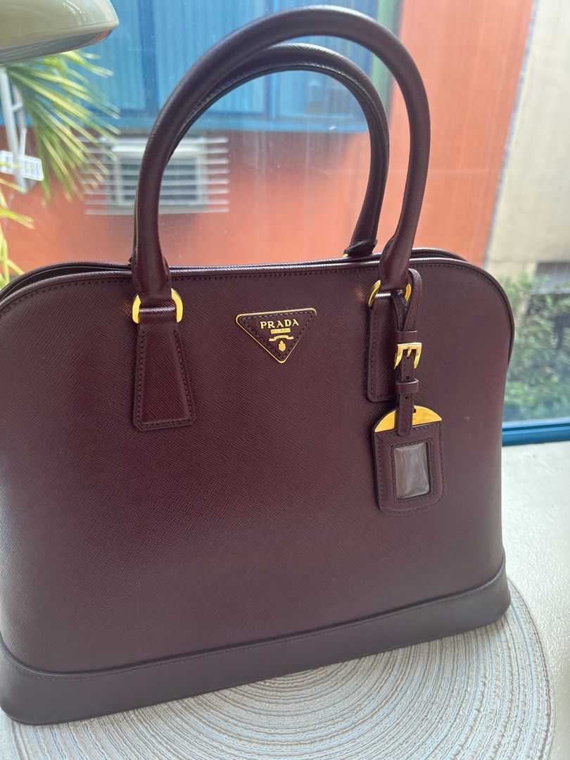 Prada Saffiano Lux tote (Category: Luxury Bags & Wallets) located in San Juan City. Submitted by iambernie (Listing ID 1366443406, Image 1). Description: The stunning promenade tote is high on appeal and style. Dazzling in a gorgeous granato (maroon )shade, the bag is crafted from saffiano leather and features 2 rolled handles and a detachable shoulder strap. The snap button leads way to a nylon lined interior with enough space for your essential