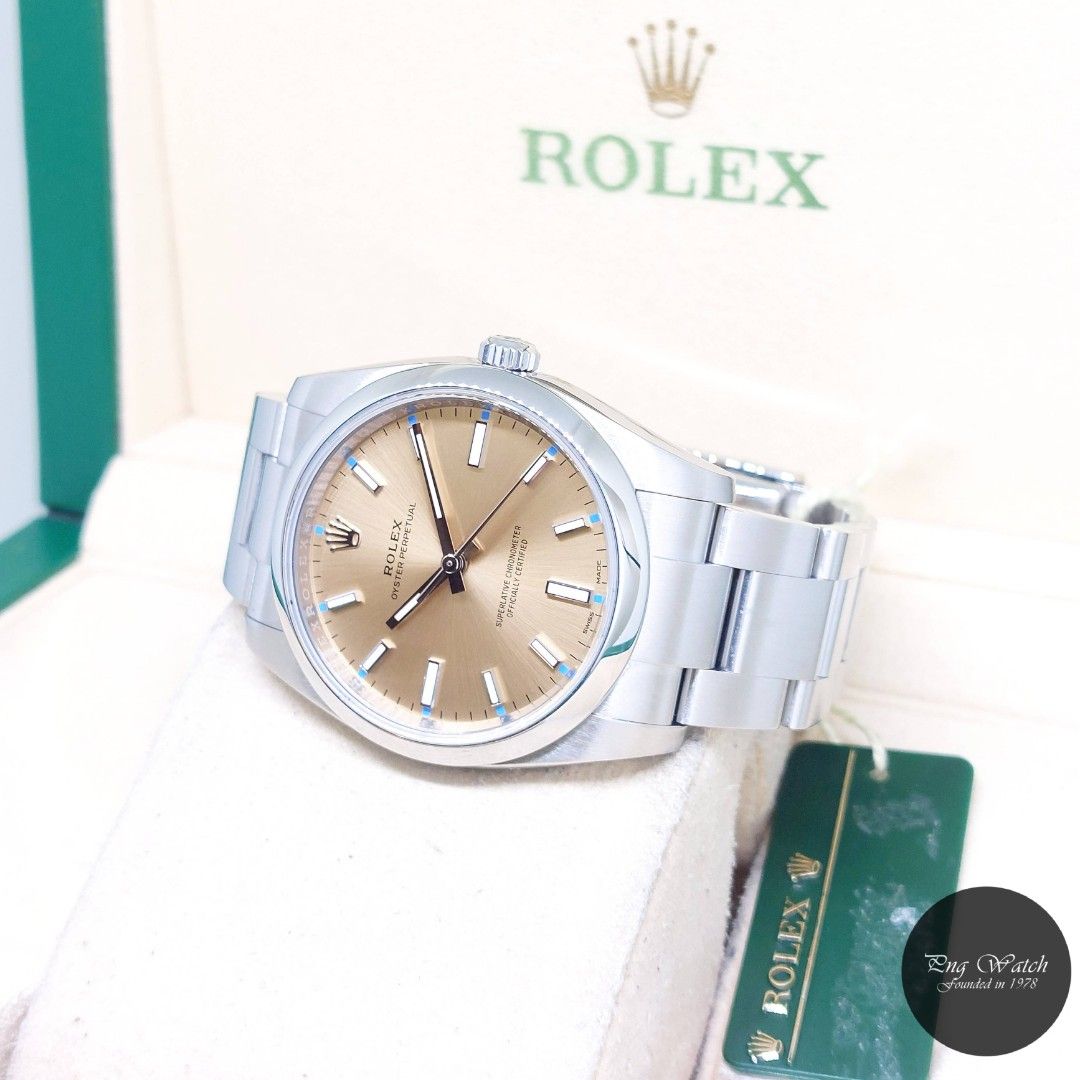 Rolex 34mm Champagne Batons Dial Oyster Perpetual REF: 114200 (Box, Card, Tag-2015) (Category: Watches) located in Singapore. Submitted by pngwatchdealer (Listing ID 1370404819, Image 2). Description: [SPECIFICATIONS] **Watch comes in full option (Box, Card & Tag)** **Straight bracelet** Brand: Rolex Model: Oyster Perpetual (REF: 114200)(AN)(15)(O) Movement: Automatic (Self-Winding) Functions and Features: Hours, Minutes and Seconds (CASE) Case M