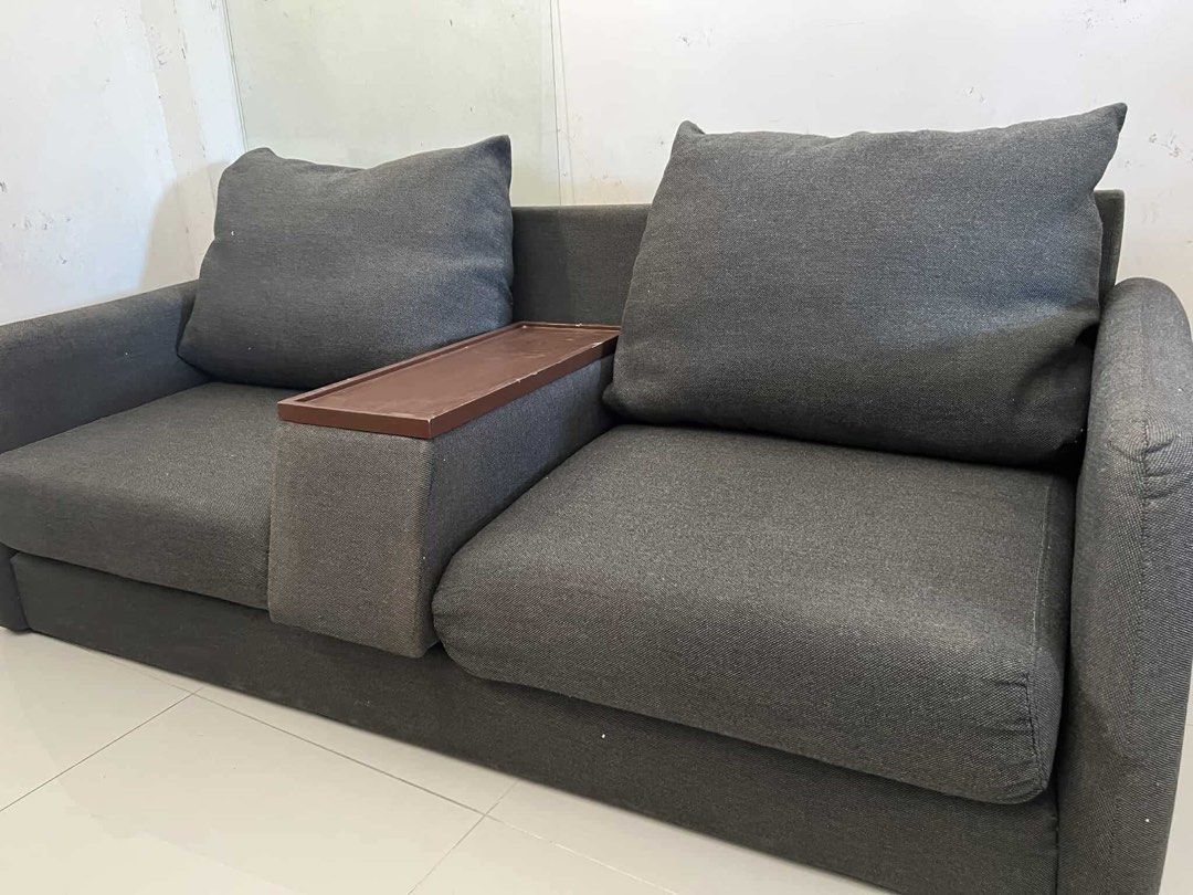 Sofa Japan Surplus (Category: Sofas) located in Makati City. Submitted by thiftdirection (Listing ID 1367388452, Image 2). Description: A compact, modern two-seater sofa with dark gray fabric upholstery. The design is minimalist, featuring straight arms and large, plush backrest cushions. A unique detail is the built-in tray or console between the two seats, likely for placing drinks or small items, enhancing its functionality for casual seating 