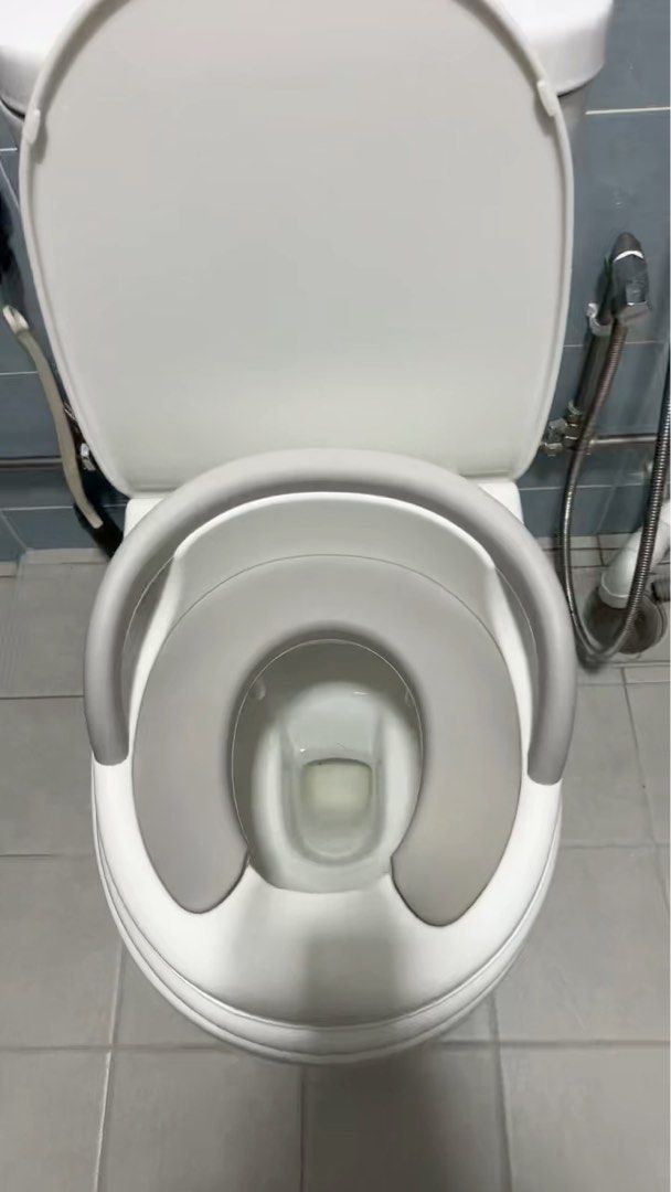 Potty Training Toilet Seat with Handles (Category: Toilet Training) located in Singapore. Submitted by jsee2212 (Listing ID 1375581398, Image 1). Description: This is a potty training toilet seat with handles. It is designed to fit on a standard toilet seat. The seat is gray and white. It has handles on both sides for the child to hold on to. It looks like it is in great condition. It is a great way to help your child transition from a potty to a
