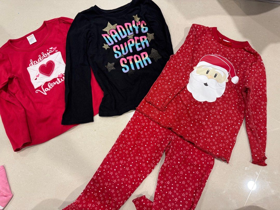 Girls' Pajama and Shirt Bundle (4-5y) (Category: Babies & Kids Fashion) located in Singapore. Submitted by joyceux (Listing ID 1377699255, Image 1). Description: Bundle of girls' long-sleeved shirts and pajama set. Includes a red Valentine's Day shirt, a black "Daddy's Super Star" shirt, and a red Christmas pajama set with a Santa Claus design. All items are in good condition. $6 postage included.