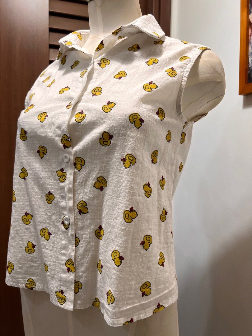 Playful Duck Print Sleeveless Shirt (Category: Shirts) located in Singapore. Submitted by minni3scloset (Listing ID 1380263997, Image 3). Description: Cheerful and lightweight, this sleeveless shirt is adorned with a fun all-over yellow duck print, perfect for casual sunny days. The button-down front and pointed collar add a touch of structure to the relaxed silhouette. Made from breathable fabric with a soft texture, it’s both cute and comfortab