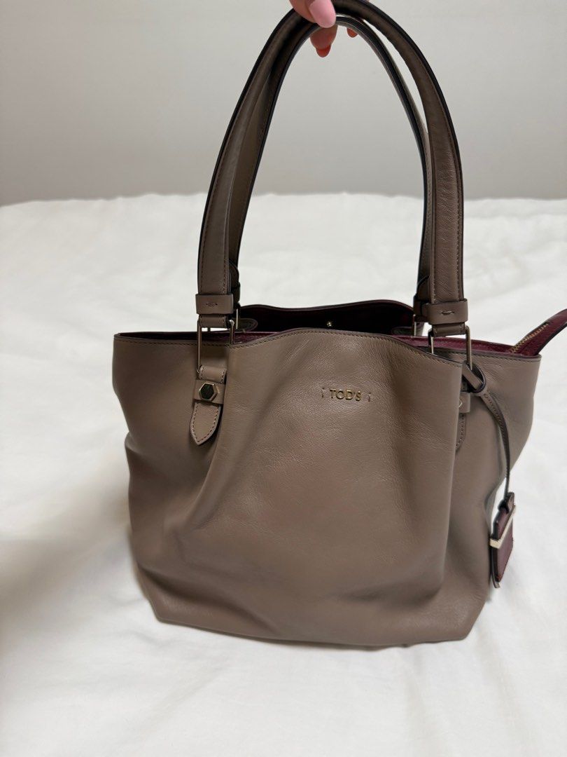 Authentic Tod's Leather Tote Bag (Category: Bags & Wallets) located in Singapore. Submitted by madisonavenue (Listing ID 1381414308, Image 1). Description: Beautiful Tod's tote bag in a lovely taupe color. Features a spacious interior with a contrasting burgundy lining. The bag has a classic design with sturdy handles and protective feet. Like new - less than 5 wears Check the photo - of 1 defect in the zipper .