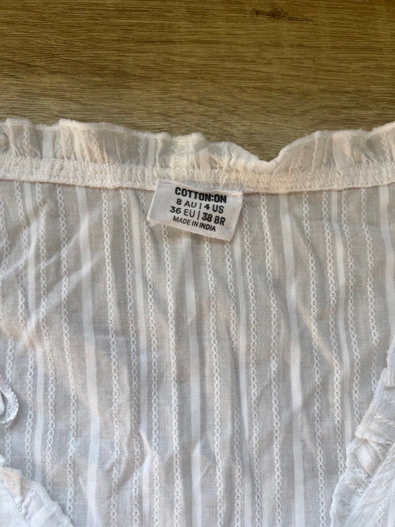 Cotton On White Tie-Front Top (Category: Sleeveless) located in Singapore. Submitted by ilovecheesefries (Listing ID 1378430575, Image 2). Description: This lovely white top from Cotton On features a tie-front design and a flattering fit. It has a delicate striped texture and ruffled detailing. Perfect for a casual, beach cover up or formal occasion! .
