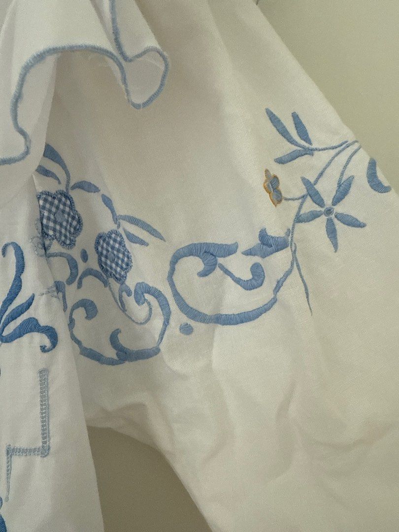 Vintage remake Embroidered White Blouse with Blue Floral Detail (Category: Blouses) located in Singapore. Submitted by jjh2019 (Listing ID 1378967326, Image 3). Description: Beautiful vintage remake white blouse with intricate blue floral embroidery. Features a unique design with ruffled sleeves and a scalloped hem. Includes a single button closure. Perfect for adding a touch of vintage charm to any outfit..