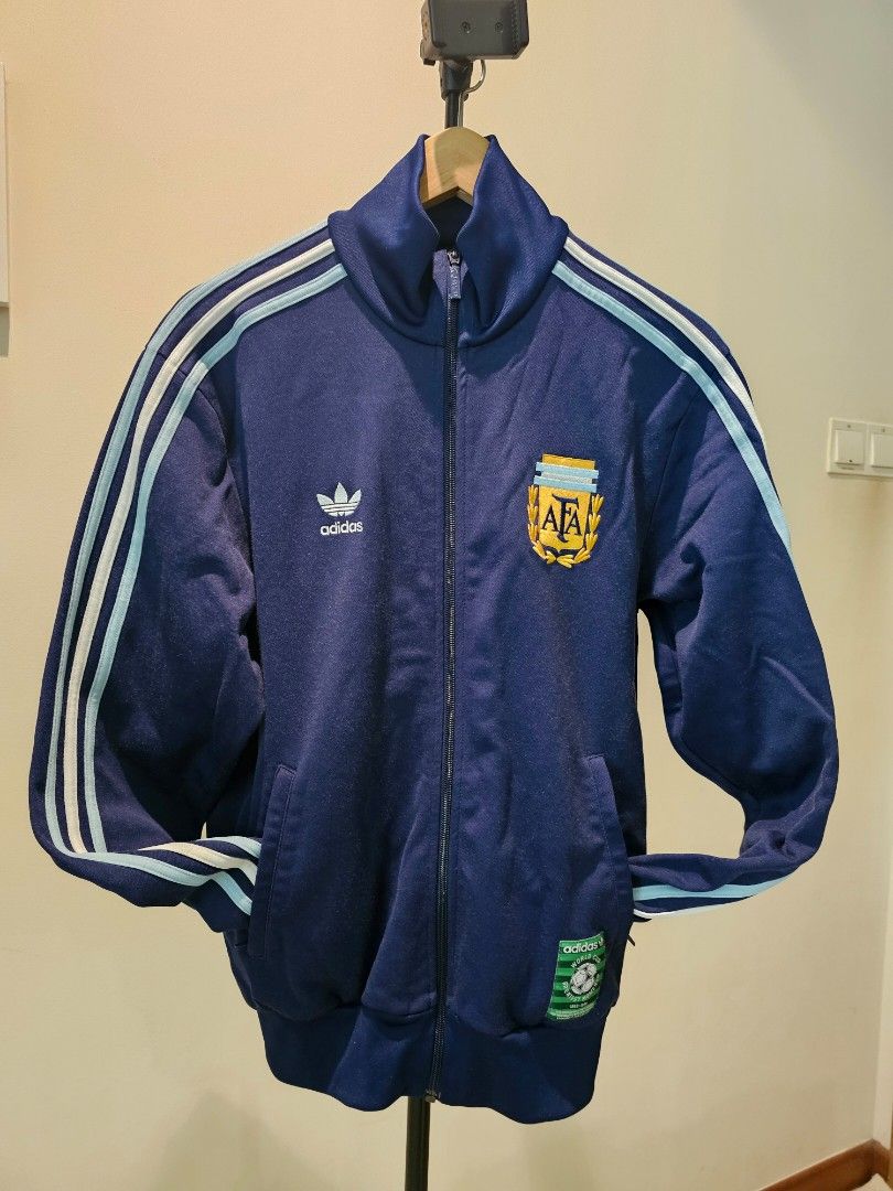 Adidas Argentina Track Jacket - Vintage (Category: Coats, Jackets and Outerwear) located in Singapore. Submitted by imagine.coffee (Listing ID 1379414690, Image 3). Description: Adidas Homage to the GOAT. Diego Armando Maradona. Hand Of God. Vintage Adidas Argentina track jacket. Features team crest, 'World Cup Moments' patch, and classic three stripes. Full zip, two pockets. Perfect for fans and vintage collectors..
