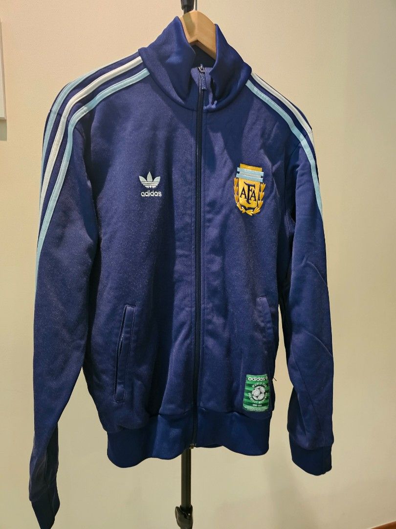 Adidas Argentina Track Jacket - Vintage (Category: Coats, Jackets and Outerwear) located in Singapore. Submitted by imagine.coffee (Listing ID 1379414690, Image 1). Description: Adidas Homage to the GOAT. Diego Armando Maradona. Hand Of God. Vintage Adidas Argentina track jacket. Features team crest, 'World Cup Moments' patch, and classic three stripes. Full zip, two pockets. Perfect for fans and vintage collectors..
