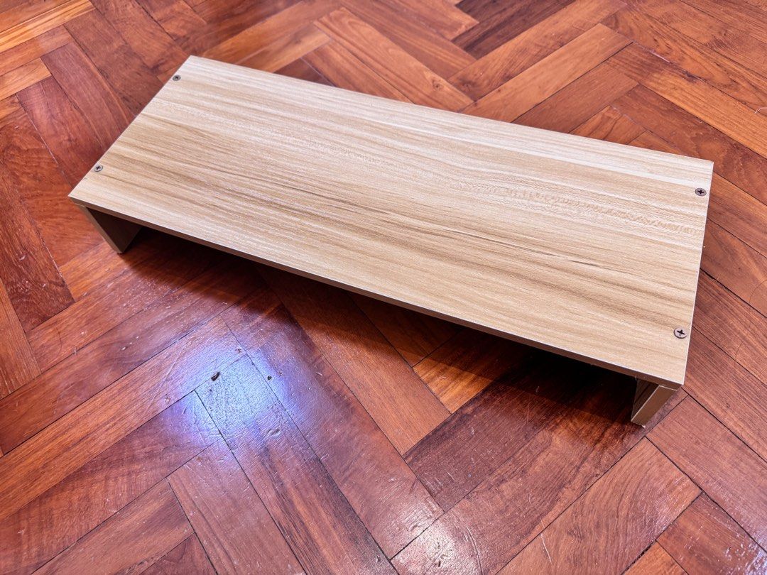 Wooden Monitor Stand - Light Brown (Category: Other Accessories) located in Singapore. Submitted by yulinng (Listing ID 1379489713, Image 3). Description: This wooden monitor is perfect for raising your monitor to a more comfortable viewing height, freeing up desk space. The light brown finish complements most desk setups. Screws are visible on the top surface. Do note that it is slightly bent in the middle..