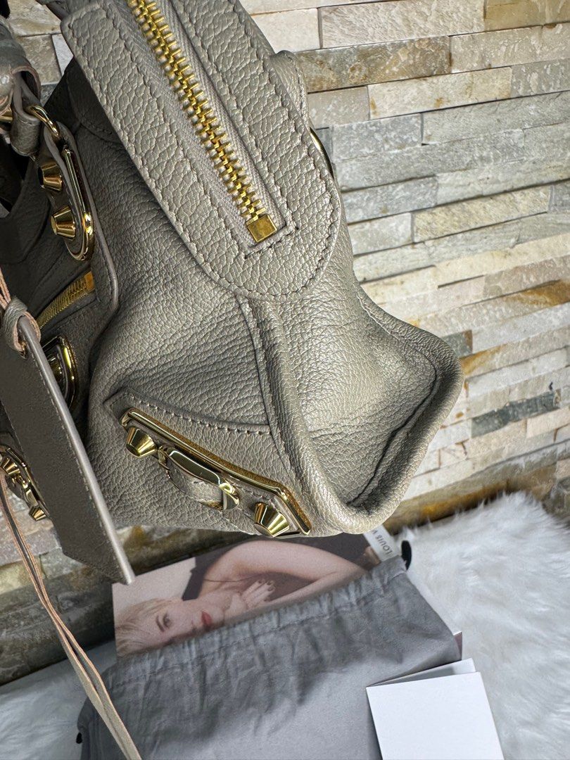 Balenciaga Mini City (Category: Luxury Bags & Wallets) located in Taguig. Submitted by angelbellaclaire (Listing ID 1386466508, Image 3). Description: Balenciaga City Bag – Mini – Taupe with Gold Hardware • Material: Premium grained lambskin leather • Color: Taupe (neutral gray-brown tone) • Hardware: Shiny gold-tone studs and zipper pulls • Features: Signature front zipper pocket, detachable leather-framed mirror, top zip closure, dual rolled le