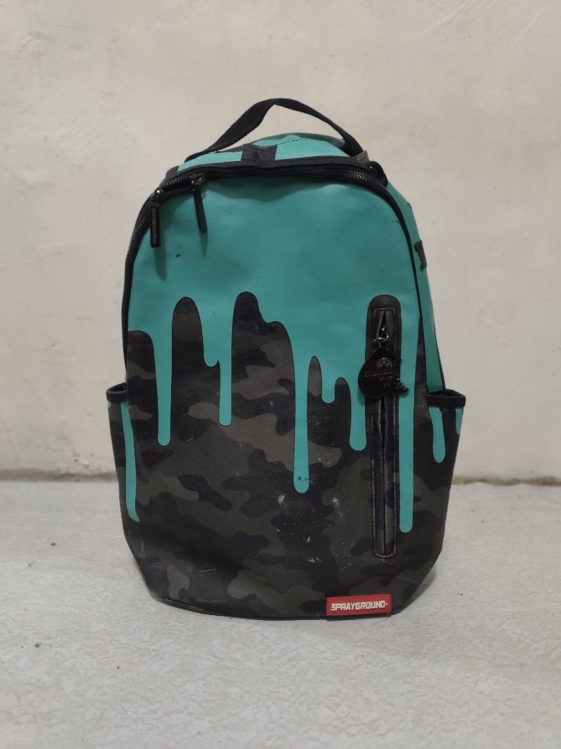 Sprayground Drip Camo Backpack (Category: Backpacks) located in Manila. Submitted by renzmalacc07450 (Listing ID 1393621571, Image 1). Description: Sprayground Tiff Drip Camo Teal Leather bought in middle east leather may mga issue na kit naman s pic baliwag bulacan 1800 - Sprayground backpack with unique drip camo design. - Teal top with black drips over a camouflage pattern. - Features multiple zippered compartments and side pockets. - Includes