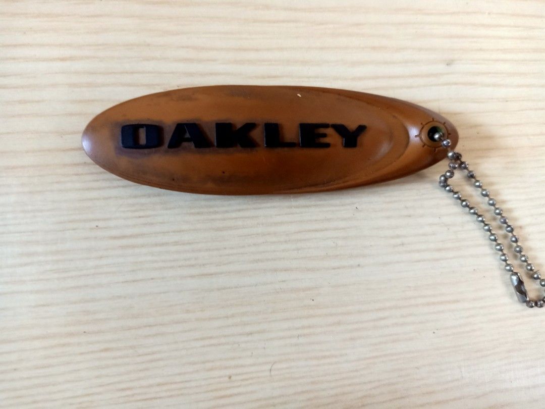 Oakley Keychain (Category: Luxury Accessories) located in Las Pinas. Submitted by the_recycle_shop (Listing ID 1394649058, Image 1). Description: - Oakley keychain - Brown oval design - Black "OAKLEY" branding - Includes metal chain - Made of durable material.
