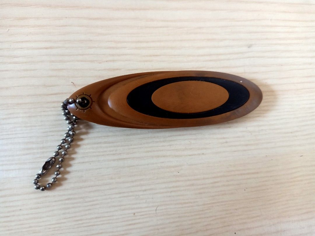 Oakley Keychain (Category: Luxury Accessories) located in Las Pinas. Submitted by the_recycle_shop (Listing ID 1394649058, Image 2). Description: - Oakley keychain - Brown oval design - Black "OAKLEY" branding - Includes metal chain - Made of durable material.