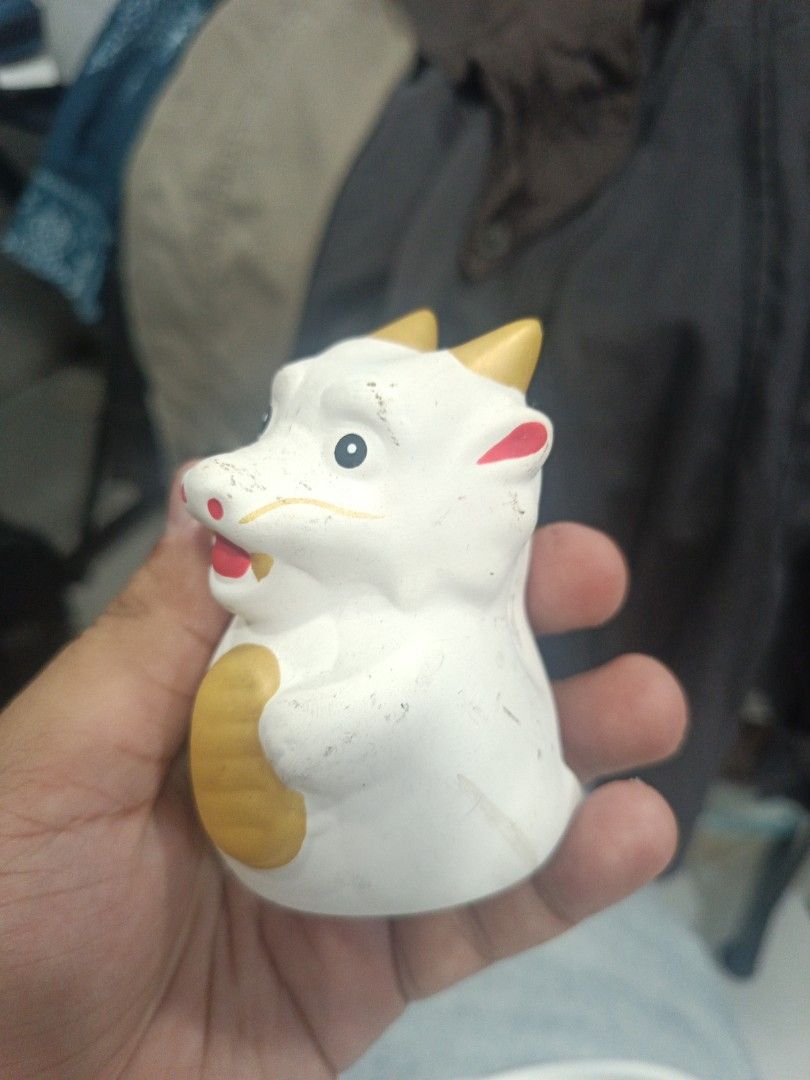 White Ceramic Lucky Dragon Figurine (Category: Other Home Decor) located in Quezon City. Submitted by bjetp (Listing ID 1394763409, Image 2). Description: - Adorable ceramic figurine - White body with gold coin and red accents - Smiling face with black eyes - Features yellow horns - Waving hand gesture - Unique and charming decorative item.