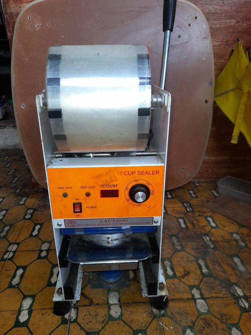 Cup Sealer Machine (Category: Other Kitchen Appliances) located in Valenzuela. Submitted by newbear.425b6e (Listing ID 1394877344, Image 1). Description: - Cup sealer machine - Orange control panel with count display - Temperature control - Power switch - Includes handle for operation - Comes with a roll of sealing film - Designed for efficient cup sealing.