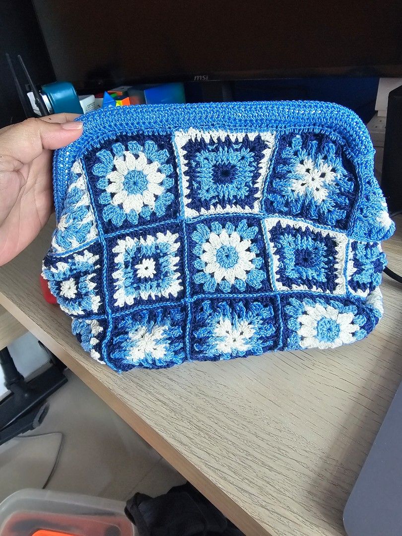 Handmade Crochet Clutch Bag - Blue (Category: Clutches) located in Makati City. Submitted by styledge.ph (Listing ID 1394874389, Image 1). Description: Handmade clutch bag features a beautiful crochet design in shades of blue and white. It has a rectangular shape with a frame closure. The bag is made of multiple crochet squares, creating a unique and stylish look. Perfect for carrying essentials, this clutch is a fashionable accessory for any occ