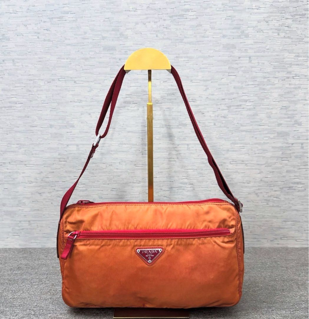 Prada Nylon Shoulder Bag (Category: Luxury Bags & Wallets) located in Quezon City. Submitted by happy_shopperrr (Listing ID 1395100330, Image 1). Description: - Prada shoulder bag - Orange nylon exterior - Red strap and trim - Prada-branded interior lining - Rectangular shape - Zip closure - Small Prada logo -with Entrupy Certificate.