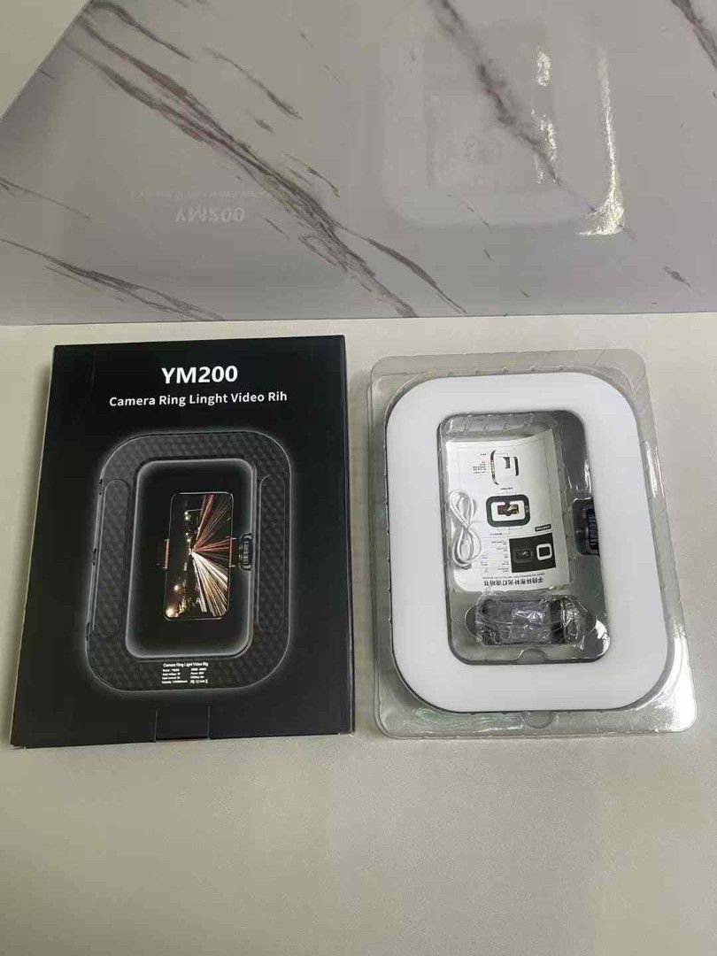 YM200 Handheld Rechargeable (8000mah)Ring Light (Category: Lighting & Studio Equipment) located in Manila. Submitted by iliasjen3082126 (Listing ID 1395130098, Image 3). Description: - YM200 Camera Ring Light for video recording - Includes: Ring light, phone holder, USB charging cable, user manual - Square-shaped ring light for bright illumination - Designed to hold your phone for easy recording - Box shows ring light with phone inside.