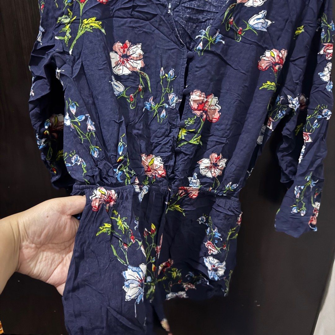 (Get 3 for 350) Elodie Floral Romper (Category: Rompers) located in Taguig. Submitted by bnplswmakeup (Listing ID 1395189197, Image 3). Description: Navy blue floral romper from Elodie. Features a V-neckline, button-down front, and long sleeves. It has an elastic waist with a drawstring. The romper is adorned with a colorful floral print. Size M-L. MOP: BPI/Gcash Shipping via J&T/Grab/Lalamove.