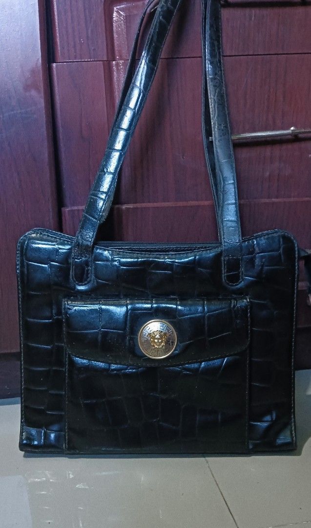 Gianni Versace Black Handbag (Category: Luxury Bags & Wallets) located in Laoag. Submitted by catrnzjb153008 (Listing ID 1395390459, Image 1). Description: - Gianni Versace handbag - Black color - Crocodile-like embossed exterior - Gold-tone Medusa head emblem on front pocket - Versace logo print interior lining - Zipper closure - Gold-tone zipper pull with Gianni Versace logo - Dual handles .