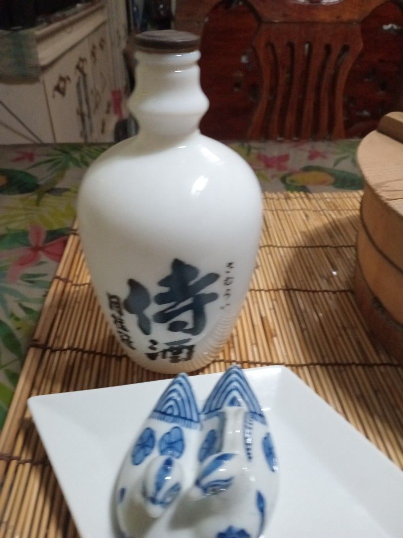 Japanese Sake Bottle and Cups Set (Category: Coffee & Tea Tableware) located in Manila. Submitted by padillahe35291 (Listing ID 1412960269, Image 2). Description: - Japanese sake set - White ceramic sake bottle with black Japanese characters - Bottle has a brown cap - Two matching white cups with blue floral patterns - Great for collectors or as a gift.