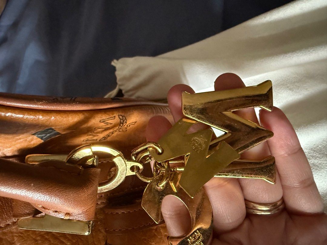 Authentic MCM Boston Bag with Charm (Category: Luxury Bags & Wallets) located in Manila. Submitted by grandeagle-f103ae (Listing ID 1414690152, Image 2). Description: - Authentic MCM Boston bag - Iconic MCM logo pattern (cognac) - Gold-tone hardware - Detachable charm - Top handle and detachable shoulder strap - Fabric lining with small pocket - Includes dust bag - Made in Korea -with free generic strap.