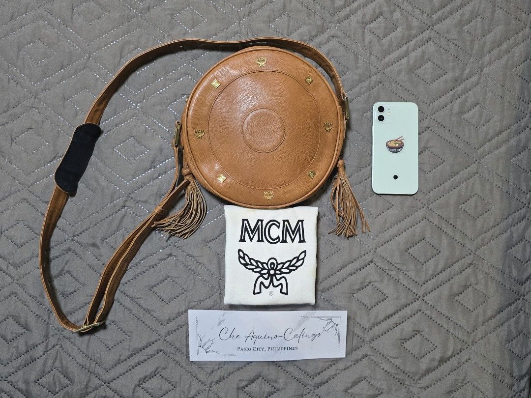 MCM Round Shoulder Bag (Category: Luxury Bags & Wallets) located in Manila. Submitted by lylmaster (Listing ID 1414799207, Image 1). Description: Authentic MCM round shoulder bag. Features a tan leather exterior with gold-tone hardware. Includes a long adjustable strap and tassel details. Comes with a dust bag. The bag has a circular design with the MCM logo embossed on the front. Perfect for everyday use..