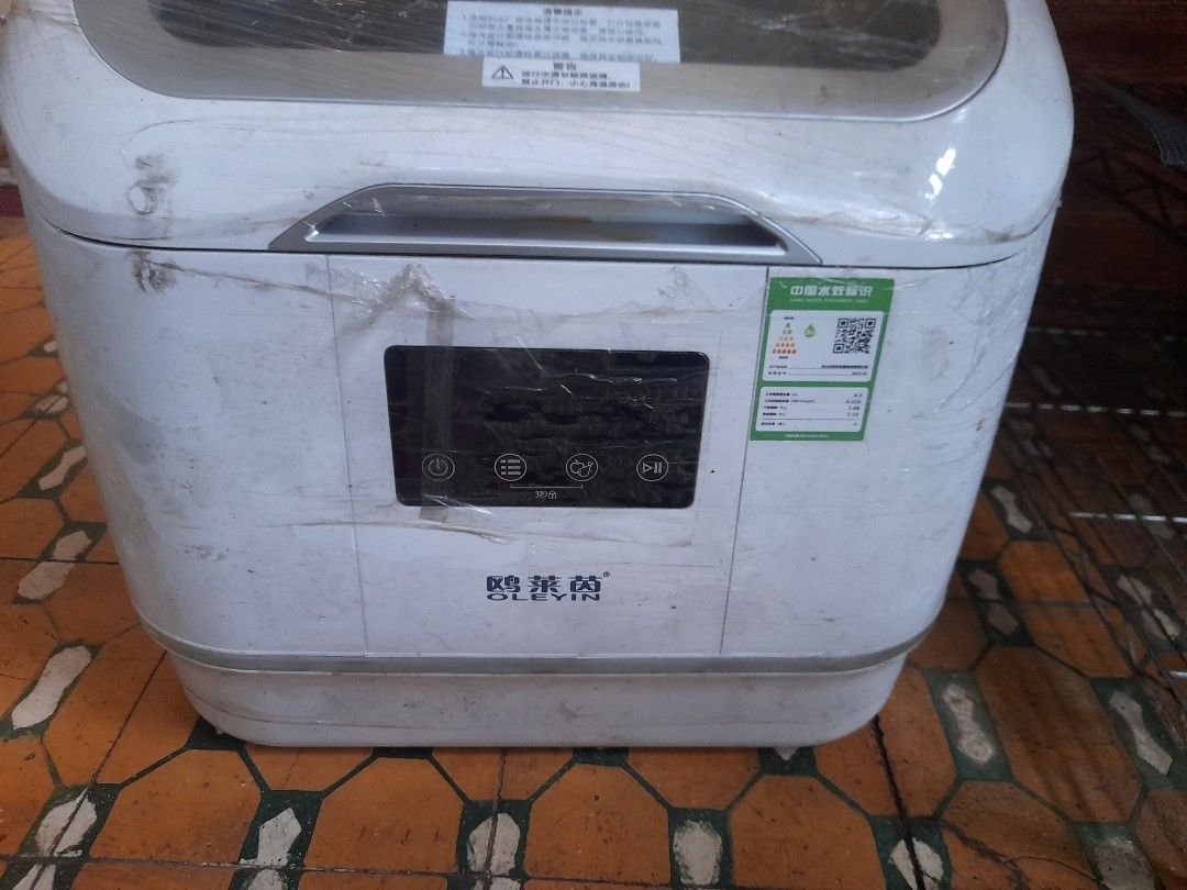 OLEVIN Dishwasher (Category: Dishwasher) located in Valenzuela. Submitted by newbear.425b6e (Listing ID 1414717295, Image 3). Description: - Includes user manual - Comes with a pack of dishwashing tablets - Features a clear door - Control panel with multiple buttons - Dish rack inside for organized washing - Includes a hose - Stylish white exterior with silver trim.