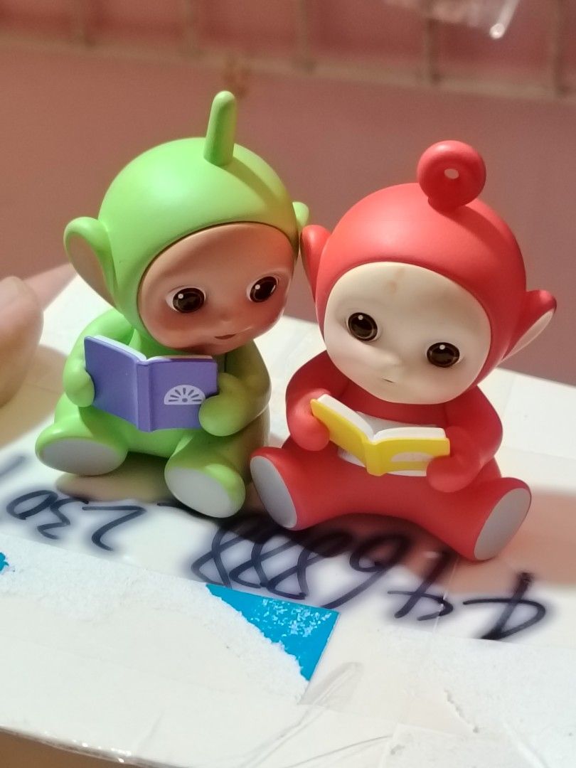 Pop Mart Teletubbies Reading Figures (Category: Designer & Blind Box Toys) located in Baguio. Submitted by ezelmix94436 (Listing ID 1414820010, Image 2). Description: - Adorable Pop Mart Teletubbies figurines - Includes two figurines: green and red Teletubbies - Each Teletubby is holding a book - Figurines are in a sitting position - Features Pop Mart and WildBrain logos - Perfect for collectors or display.