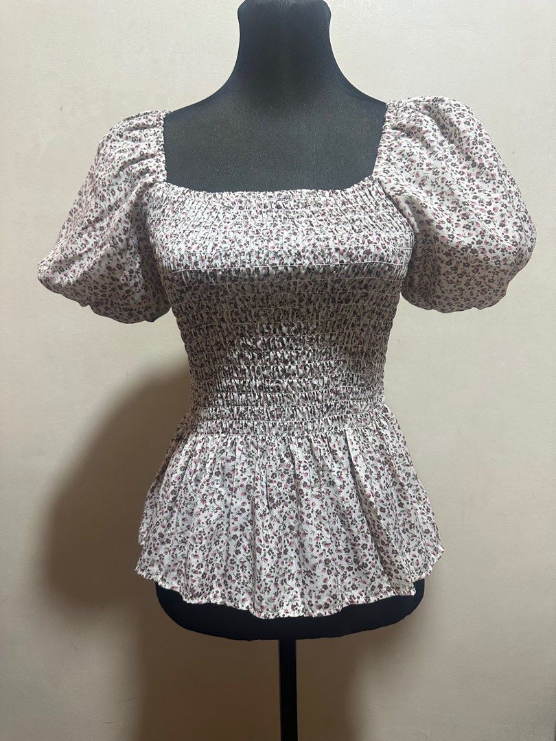 Floral Square Neck Top (Category: Blouses) located in Taguig. Submitted by sassythrifter (Listing ID 1415146222, Image 1). Description: Top features a square neckline and short puff sleeves. It has a fitted bodice with a smocked design and a peplum hem. The fabric is white with a delicate floral print in shades of purple and green. It is a stylish piece suitable for various occasions..