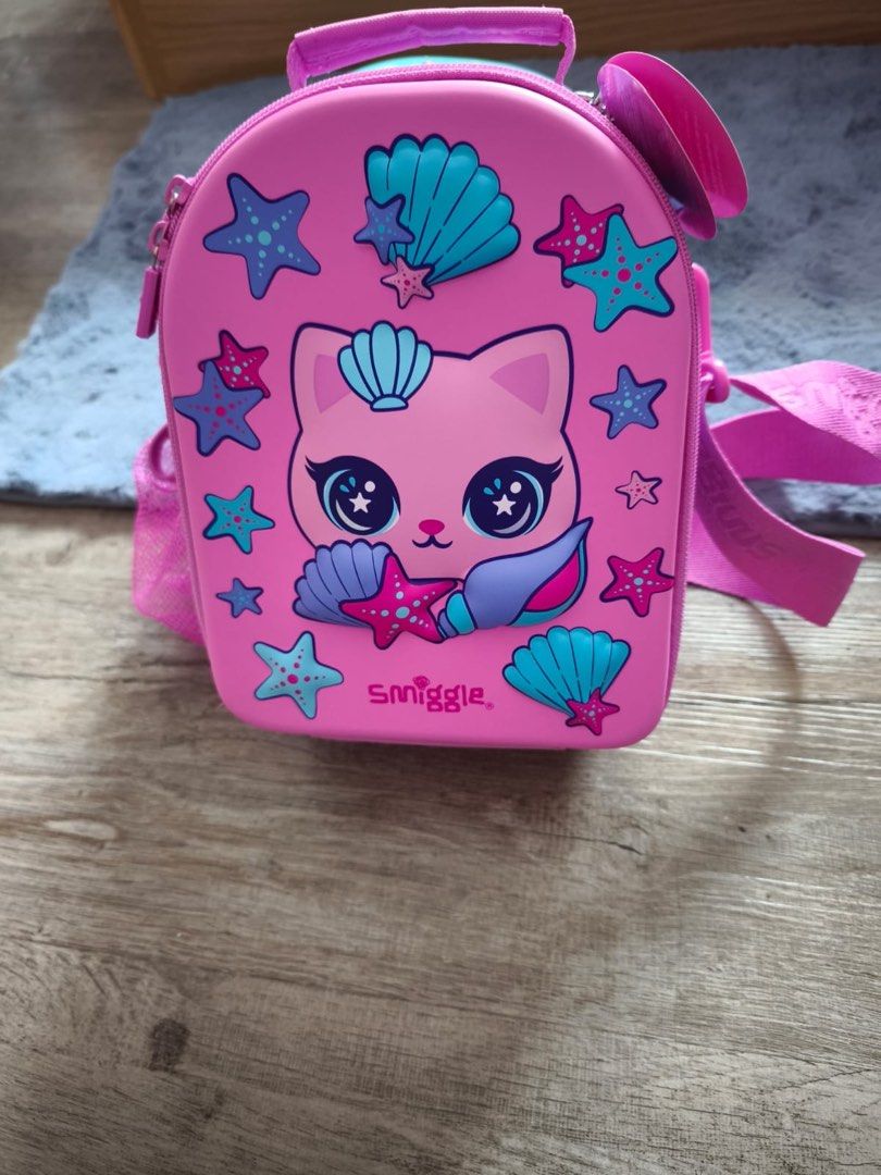 Smiggle Mermaid Cat Lunchbox with strap (Category: Babies & Kids Fashion) located in Singapore. Submitted by hola.sg (Listing ID 1415099800, Image 1). Description: - Adorable Smiggle crossbody bag - Features a fun mermaid cat design - Perfect for carrying essentials - Includes a shoulder strap and top handle.