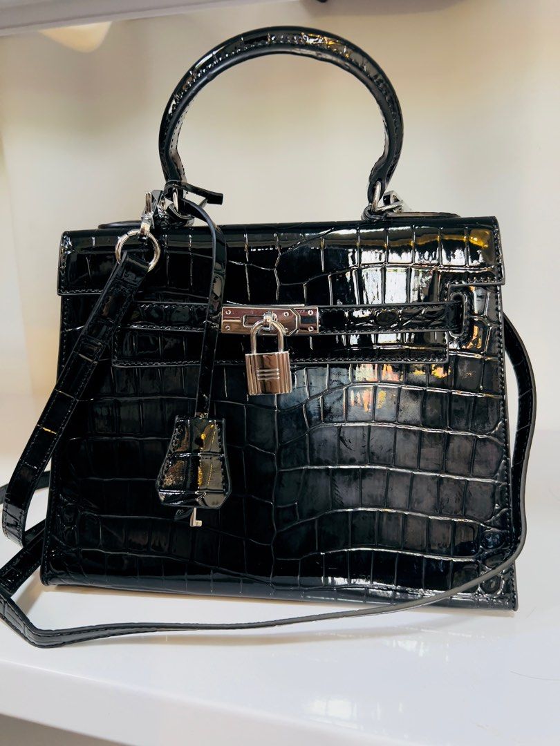 Black Crocodile-Embossed Handbag with Top Handle (Category: Luxury Bags & Wallets) located in Candelaria. Submitted by sac_du_jour (Listing ID 1415320145, Image 3). Description: - Black handbag with crocodile-embossed finish - Top handle and detachable shoulder strap - Silver-tone lock closure and hardware - Structured shape - Glossy material - Includes a small charm.
