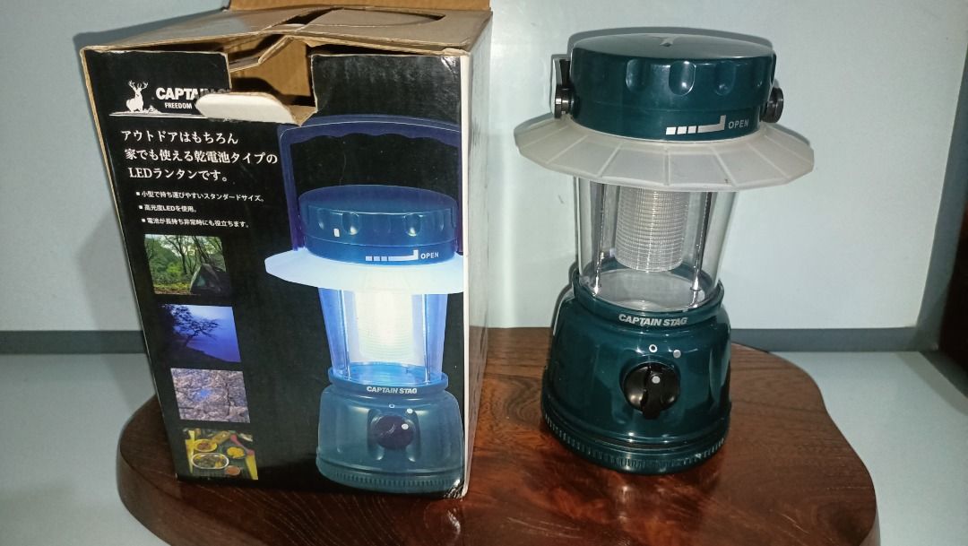 Captain Stag LED Lantern for Camping (Category: Lighting) located in Munoz. Submitted by larryc1212 (Listing ID 1415321461, Image 1). Description: Captain Stag LED lantern. The lantern is dark green with a clear lamp cover. It has an adjustable knob and a handle. The box shows the lantern's features and some example usage scenarios. The lantern is approximately 8 inches tall. This is battery operated. Item may or may not include some scratches du