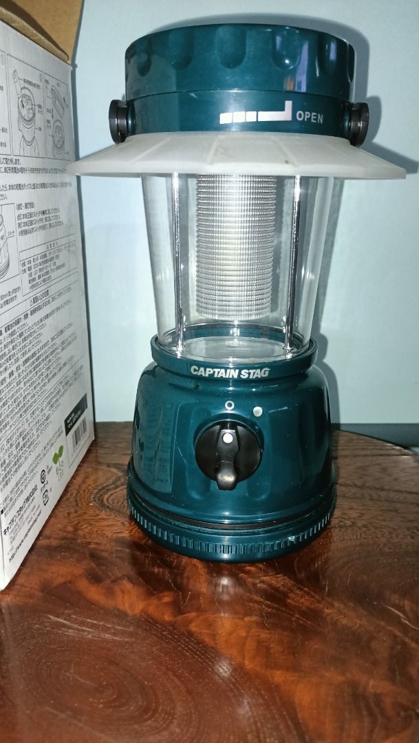 Captain Stag LED Lantern for Camping (Category: Lighting) located in Munoz. Submitted by larryc1212 (Listing ID 1415321461, Image 2). Description: Captain Stag LED lantern. The lantern is dark green with a clear lamp cover. It has an adjustable knob and a handle. The box shows the lantern's features and some example usage scenarios. The lantern is approximately 8 inches tall. This is battery operated. Item may or may not include some scratches du