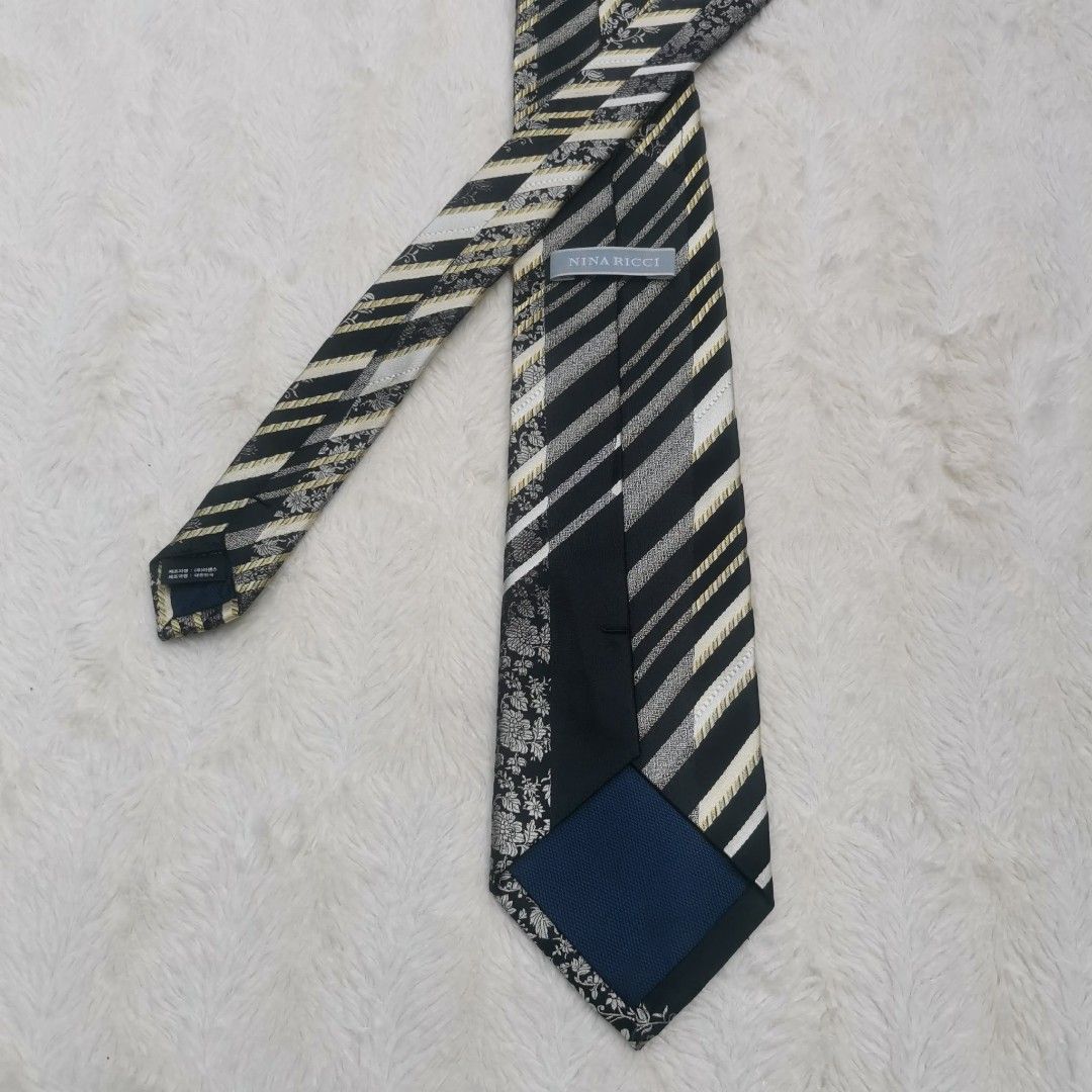 Nina Ricci Silk Tie (Category: Ties) located in Manila. Submitted by titojay (Listing ID 1415456560, Image 1). Description: Elegant Nina Ricci tie featuring a striking combination of black, white, and gold stripes with floral accents. The tie has a classic design with a standard width. The label is visible, confirming the brand. Perfect for adding a touch of sophistication to any outfit..