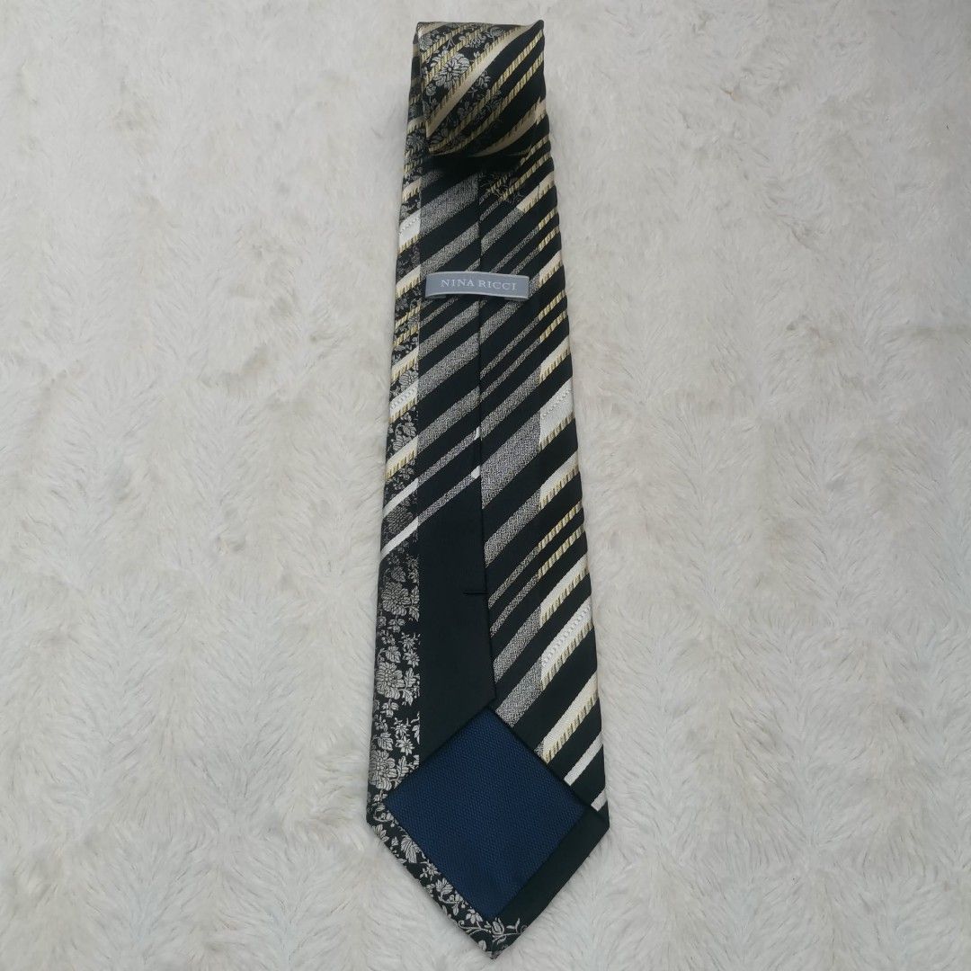 Nina Ricci Silk Tie (Category: Ties) located in Manila. Submitted by titojay (Listing ID 1415456560, Image 2). Description: Elegant Nina Ricci tie featuring a striking combination of black, white, and gold stripes with floral accents. The tie has a classic design with a standard width. The label is visible, confirming the brand. Perfect for adding a touch of sophistication to any outfit..