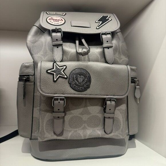 Coach Patchwork Backpack (Category: Luxury Bags & Wallets) located in Manila. Submitted by santosrich_419 (Listing ID 1415872672, Image 1). Description: - Stylish grey Coach backpack - Features multiple patches - Drawstring closure with buckle straps - Multiple pockets for storage - Coach logo pattern - Padded back for comfort - Top handle - Adjustable shoulder straps - Mix of textures and embellishments.