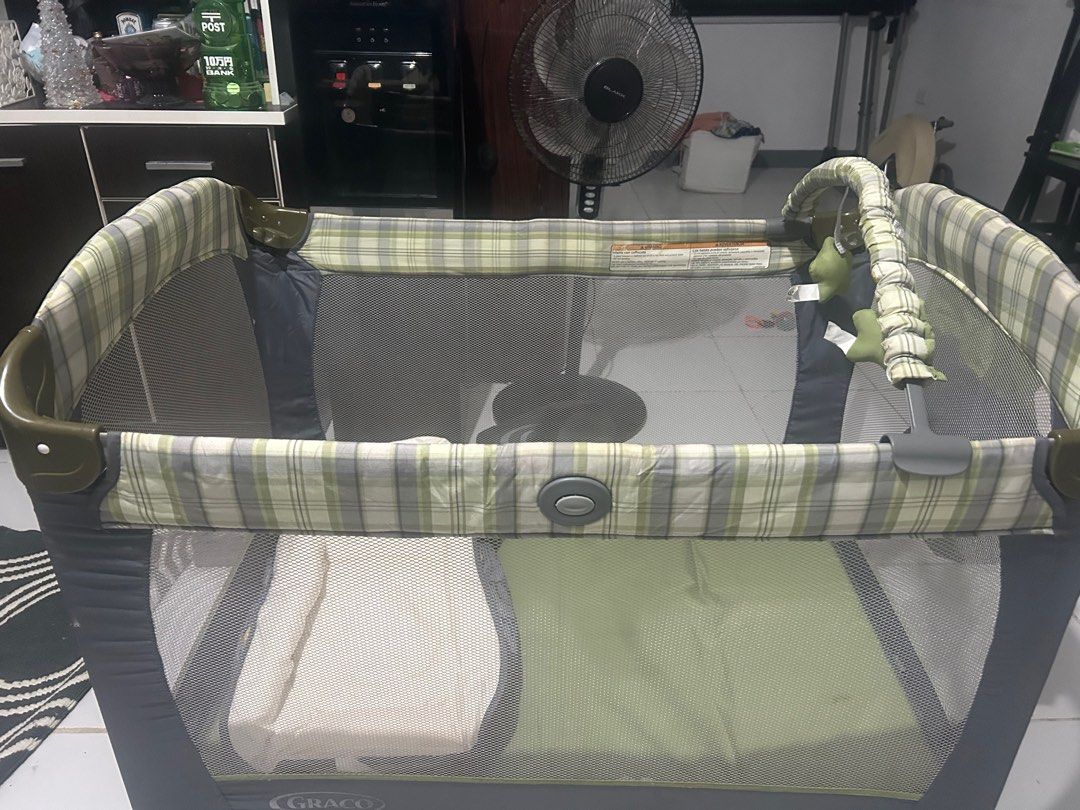 Graco Playard with Bassinet (Category: Cots & Cribs) located in San Fernando. Submitted by kimkant06043026 (Listing ID 1415823220, Image 2). Description: Graco playard with bassinet and accessories. Includes a bassinet insert, canopy with toys, and a carrying bag. The playard features a green and plaid design. The owner's manual is included..
