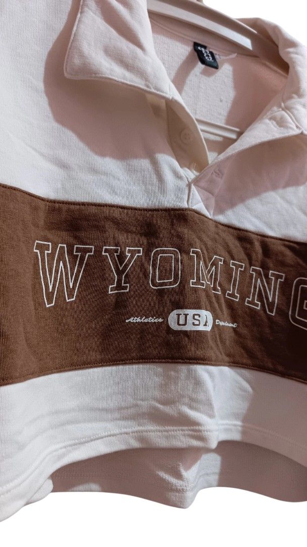 H&M Wyoming Cropped Sweatshirt (Category: Longsleeves) located in Taguig. Submitted by RetroStella (Listing ID 1415988208, Image 2). Description: - H&M cropped sweatshirt - Collared neckline - Brown chest panel with "WYOMING USA" embroidery - White sleeves and body with brown accents - Long sleeves - Relaxed fit.