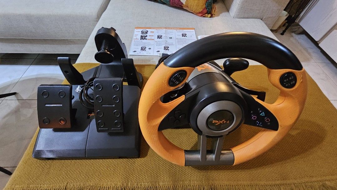 PXN V3II Gaming Steering Wheel with Pedals (Category: Controllers) located in Cebu City. Submitted by mjpashion (Listing ID 1415867862, Image 2). Description: - PXN V3II gaming steering wheel with pedals. - Stylish orange and black design. - Includes all accessories: steering wheel, pedals, and mounting hardware. - Comes with original manuals. - Perfect for enhancing your racing game experience!.