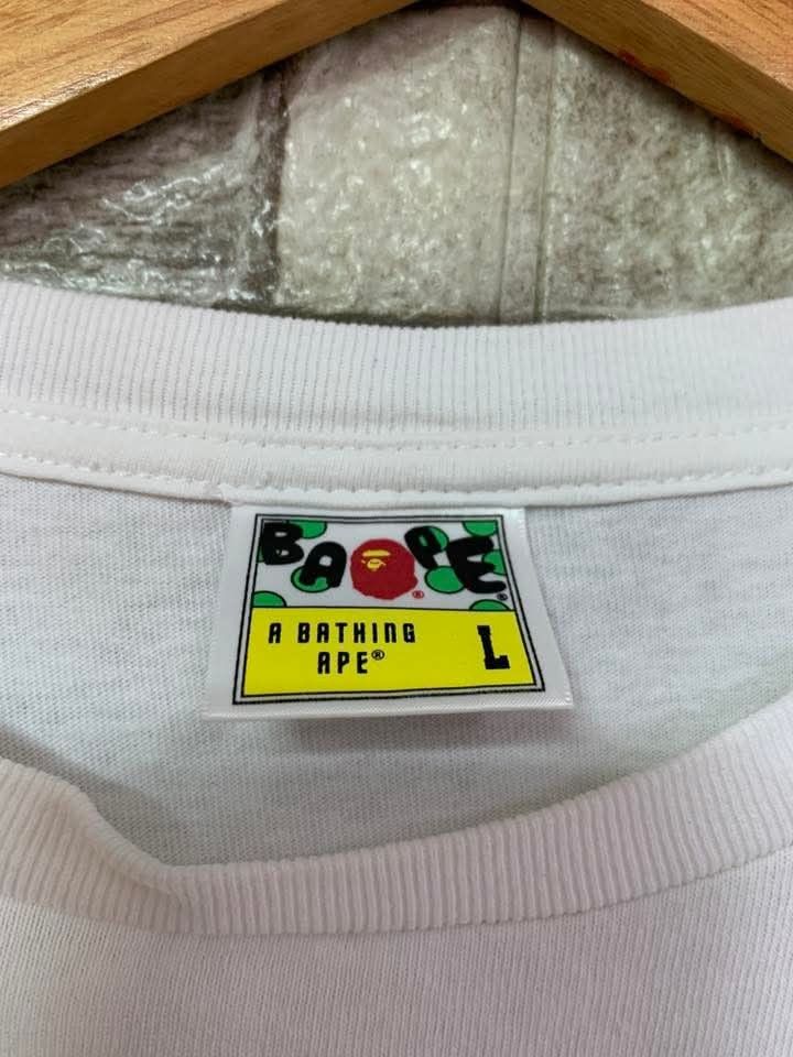 BAPE Tiger Graphic T-shirt - Large (Category: Tshirts & Polo Shirts ) located in Caloocan City. Submitted by vintstreets (Listing ID 1416174092, Image 2). Description: BAPE • Dimes: width: 21 Length: 26.5 • Condition & Color rate: 9.2/10 • no side stich • minimal hairline sa print (hindi visible) • solid din to 📥📥 📍 South Caloocan 🚚 JNT - White BAPE T-shirt - Features a tiger graphic - Crew neck and short sleeves - BAPE logo detail - Size: La