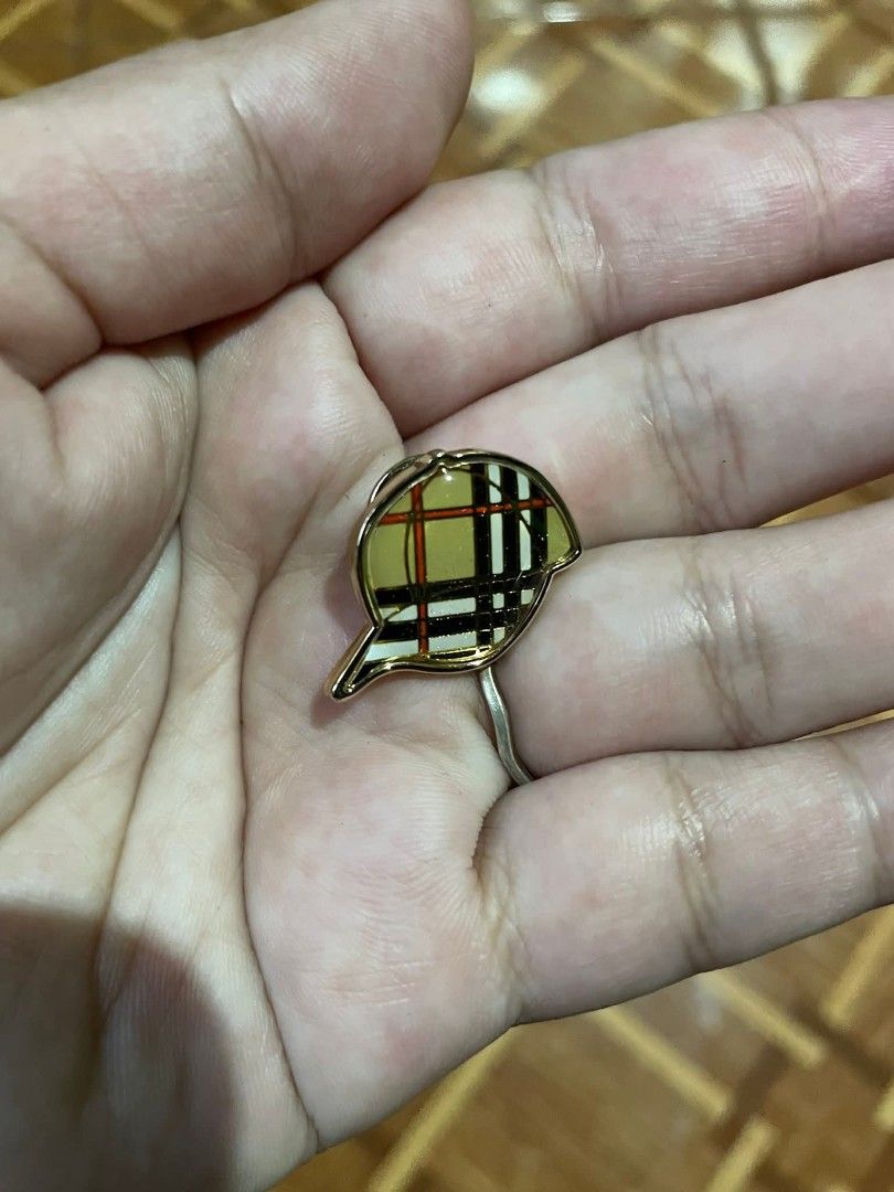 Burberry brooch/pin (Category: Luxury Accessories) located in Baguio. Submitted by cleverlion_e92944 (Listing ID 1416010096, Image 1). Description: Burberry pin features a cap design with the brand's signature check pattern. The pin has a gold-tone finish. The back of the pin is marked with the Burberry logo. It comes with a pin backing for secure attachment..