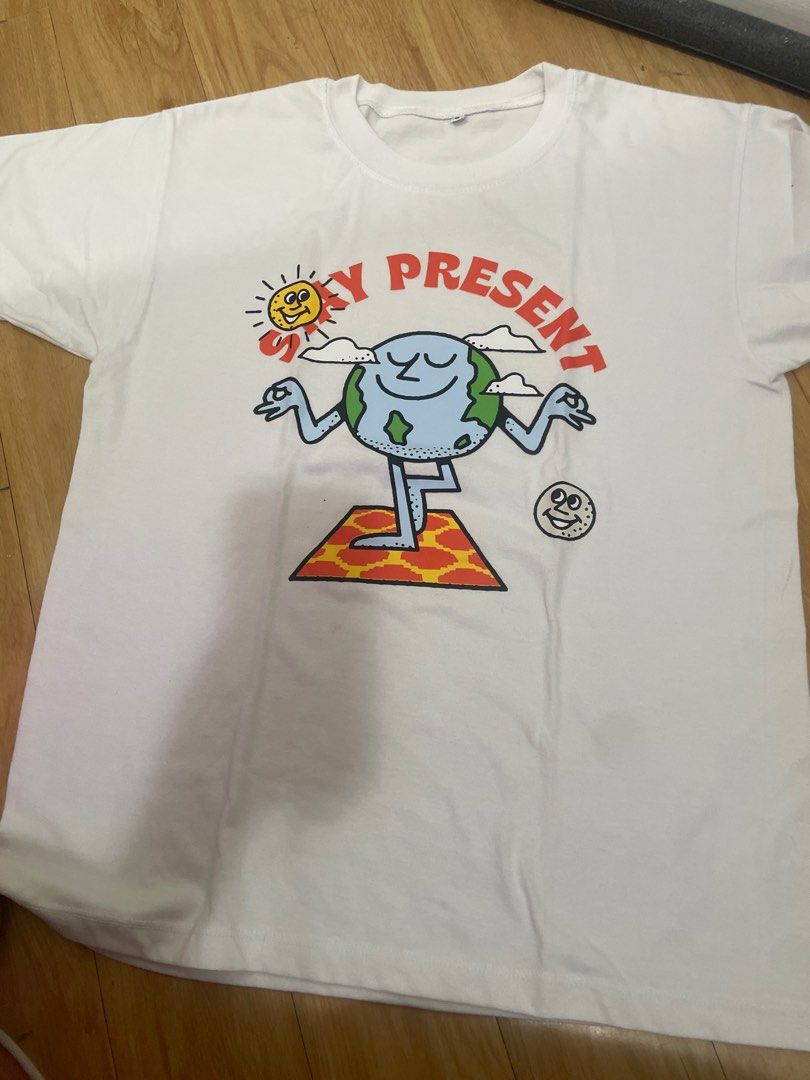 White Stay Present Graphic T-shirt (Category: Tshirts & Polo Shirts ) located in Manila. Submitted by kokocrunchmuncher (Listing ID 1416140684, Image 1). Description: - White t-shirt - Features a colorful "Stay Present" graphic - Graphic: Cartoon earth doing yoga - Crew neck - Short sleeves - Plain white back.