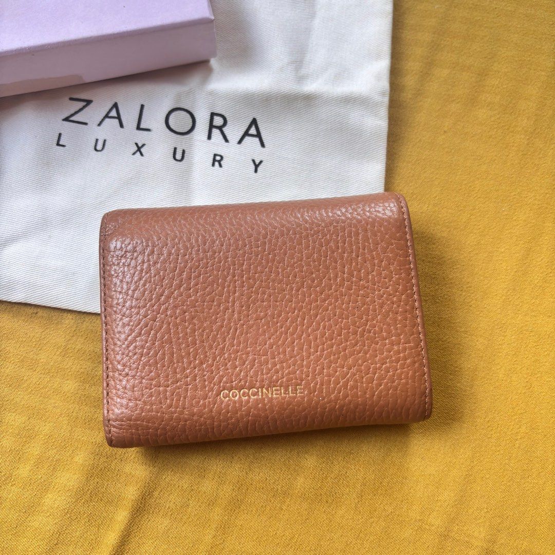 Coccinelle Small Compact Brown Leather Wallet (Category: Luxury Bags & Wallets) located in Balanga. Submitted by heyyletsdeclutter (Listing ID 1416275028, Image 3). Description: Coccinelle leather wallet in a warm brown color. Features a magnetic flap closure with a unique design. Includes a coin purse and multiple card slots. Comes with its original box and dust bag from Zalora Luxury..