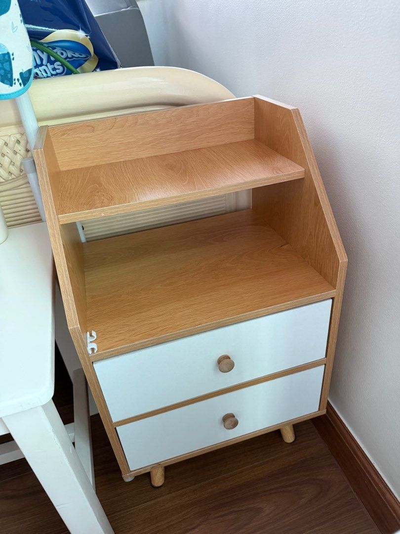 Wooden Nightstand with Drawers bedside table (Category: Shelves, Cabinets & Racks) located in Manila. Submitted by kristielyntan (Listing ID 1416313976, Image 2). Description: - Stylish wooden nightstand - Two drawers and an open shelf - Light wood finish with white drawer fronts - Unique angled design - Wooden knobs - Perfect for bedroom or living space - Adds a touch of modern design RFS: relocation.
