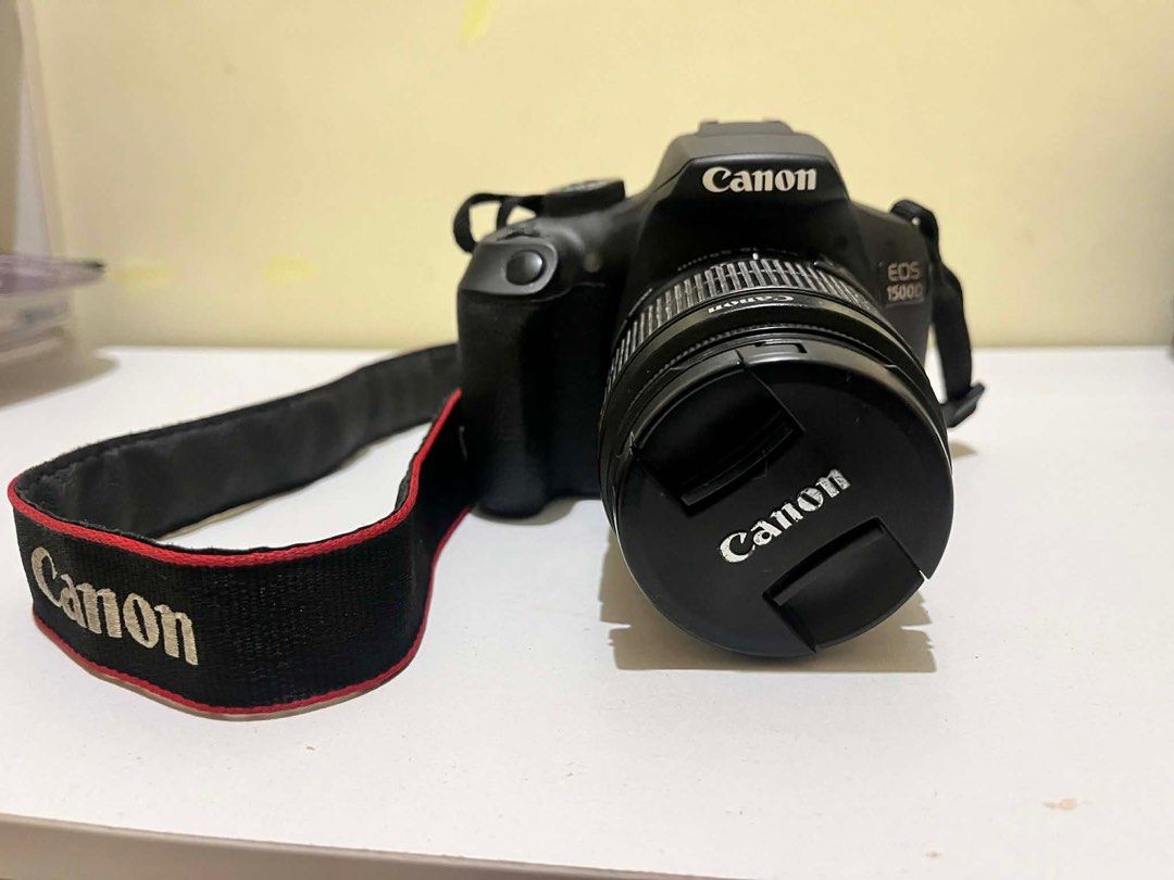 Canon EOS 1500D DSLR Camera with Lens (Category: Cameras) located in Tabuk. Submitted by iinnkk (Listing ID 1416574943, Image 1). Description: - Canon EOS 1500D DSLR Camera - Includes EF-S 18-55mm lens - Comes with lens cap, charger, and strap, camera original box - Black camera body - Features a display screen and various setting buttons - Has HDMI and other ports - Lens diameter: 58mm - Includes Canon strap ISSUE: NO COVER ON USB PORTS (SEE LAS