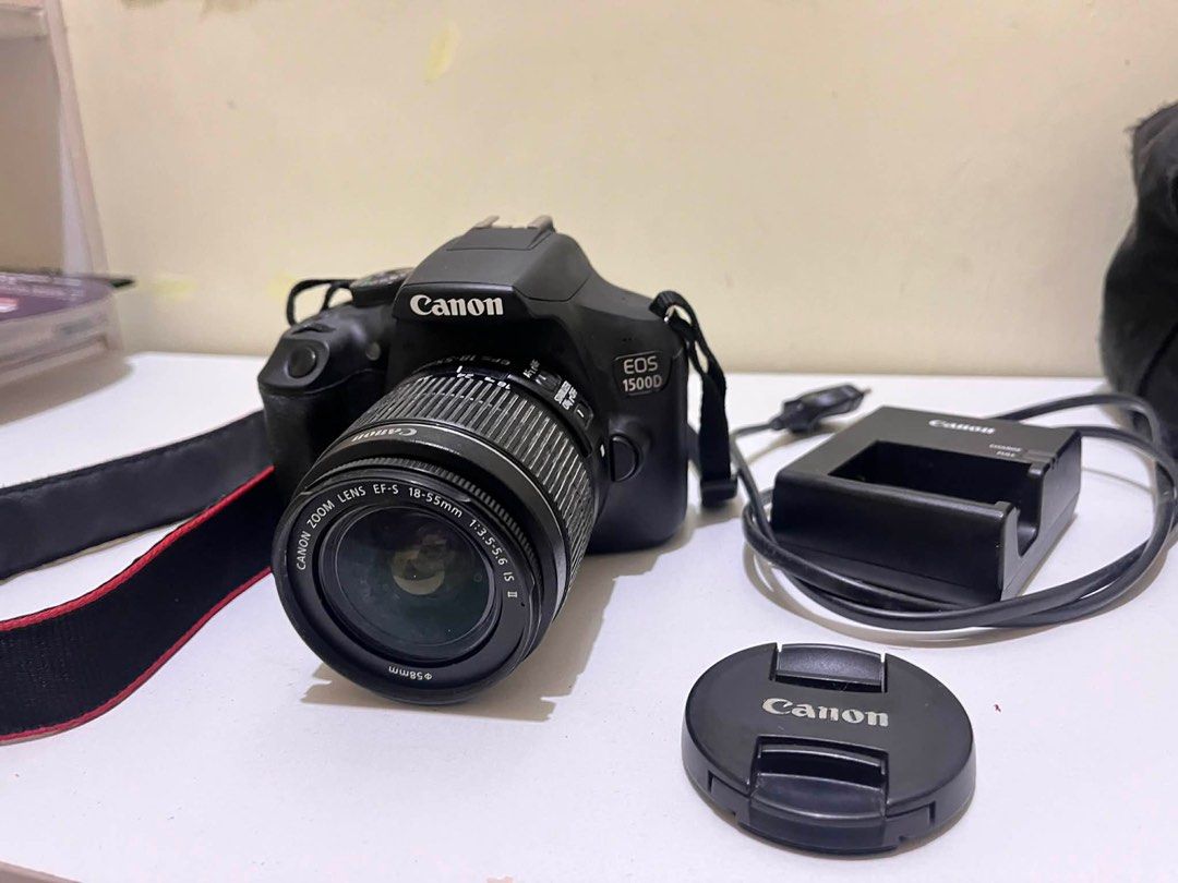 Canon EOS 1500D DSLR Camera with Lens (Category: Cameras) located in Tabuk. Submitted by iinnkk (Listing ID 1416574943, Image 2). Description: - Canon EOS 1500D DSLR Camera - Includes EF-S 18-55mm lens - Comes with lens cap, charger, and strap, camera original box - Black camera body - Features a display screen and various setting buttons - Has HDMI and other ports - Lens diameter: 58mm - Includes Canon strap ISSUE: NO COVER ON USB PORTS (SEE LAS