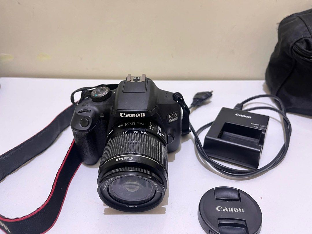 Canon EOS 1500D DSLR Camera with Lens (Category: Cameras) located in Tabuk. Submitted by iinnkk (Listing ID 1416574943, Image 3). Description: - Canon EOS 1500D DSLR Camera - Includes EF-S 18-55mm lens - Comes with lens cap, charger, and strap, camera original box - Black camera body - Features a display screen and various setting buttons - Has HDMI and other ports - Lens diameter: 58mm - Includes Canon strap ISSUE: NO COVER ON USB PORTS (SEE LAS