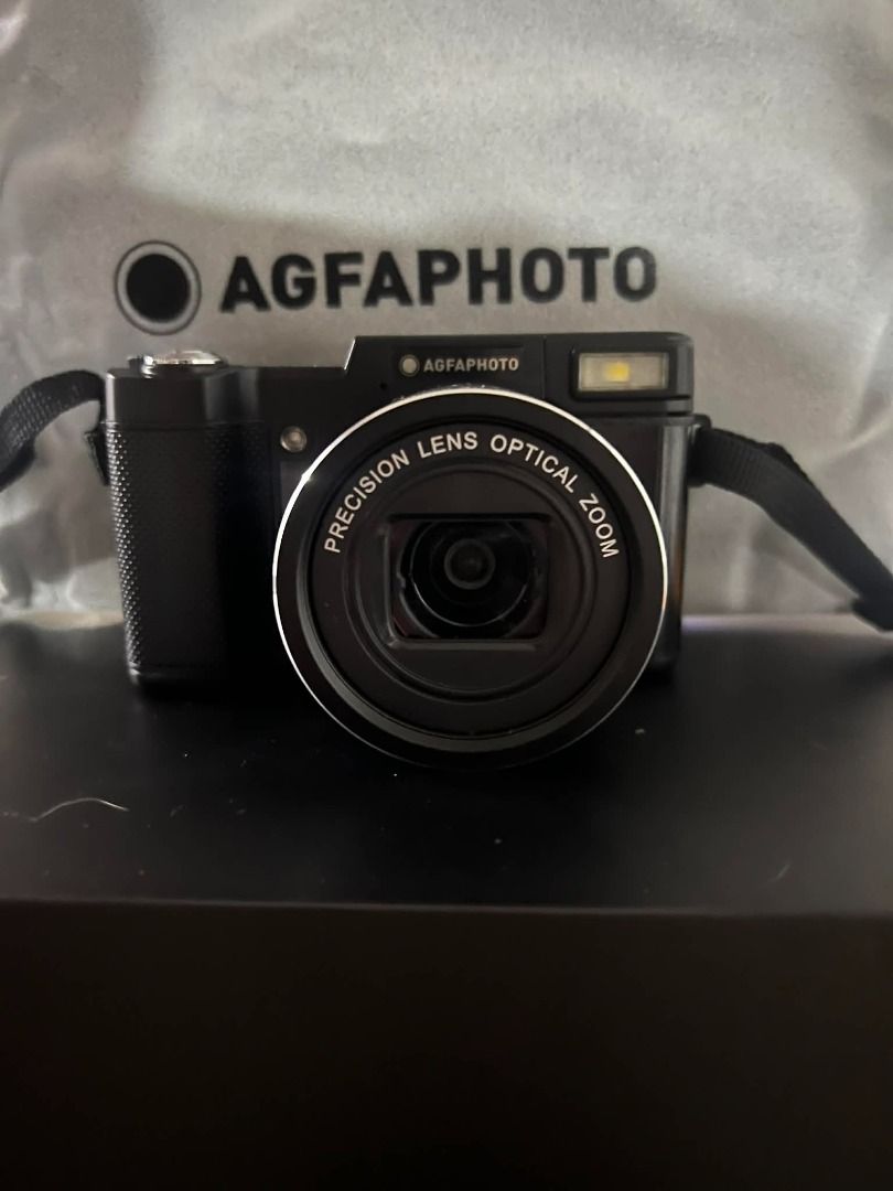 AGFAPHOTO Realishot VLG-4K OPT Digital Camera (Category: Cameras) located in Pasig City. Submitted by jcarevalo (Listing ID 1416927351, Image 3). Description: AGFAPHOTO Realishot VLG-4K OPT digital camera. Includes a microphone, user manual, and other accessories. Features a precision lens with optical zoom. The camera has a built-in flash and a flip-up screen. Comes with a carrying strap and a protective cloth. The camera is black. - BRANDNEW - 