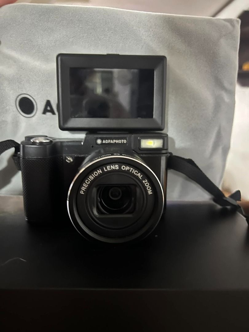 AGFAPHOTO Realishot VLG-4K OPT Digital Camera (Category: Cameras) located in Pasig City. Submitted by jcarevalo (Listing ID 1416927351, Image 2). Description: AGFAPHOTO Realishot VLG-4K OPT digital camera. Includes a microphone, user manual, and other accessories. Features a precision lens with optical zoom. The camera has a built-in flash and a flip-up screen. Comes with a carrying strap and a protective cloth. The camera is black. - BRANDNEW - 
