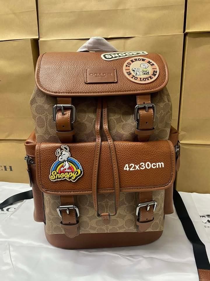Coach Snoopy Patchwork Backpack (Category: Luxury Bags & Wallets) located in Manila. Submitted by santosrich_419 (Listing ID 1416998724, Image 1). Description: Coach backpack features a brown leather and signature canvas design with Snoopy patches. It has multiple pockets, including a front zippered pocket and side pockets. The backpack has adjustable straps and a drawstring closure. Dimensions are approximately 42x30cm..